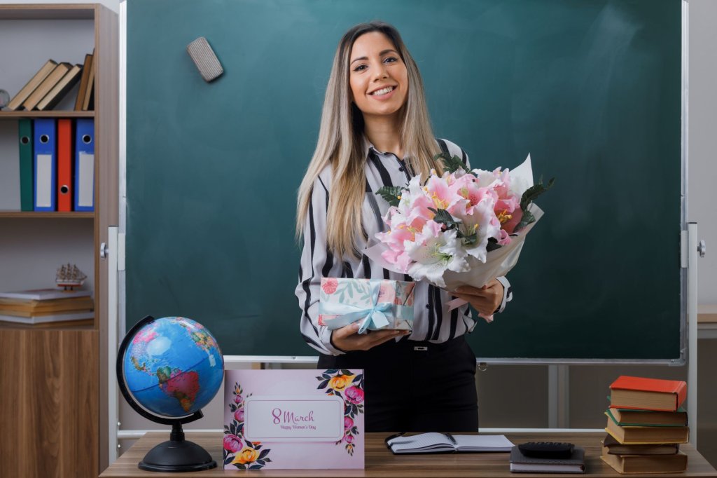 molodaa-zensina-ucitel-stoasaa-u-doski-v-klasse-derzasaa-buket-cvetov-i-podarocnuu-korobku-ot-studentov-vygladasaa-scastlivoi-i-dovol-noi-koncepciei-scastlivogo-zenskogo-dna.jpg